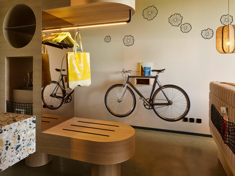 Modern room with wooden furniture, a bicycle mounted on the wall, a hanging yellow bag, and flower decals on a light-colored wall—perfect for relaxing or getting inspired after a busy 25hours.