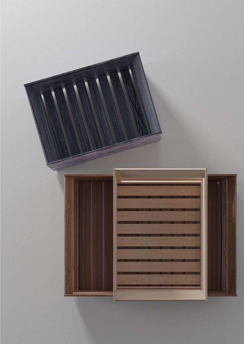 Three empty rectangular wooden crates in different shades are arranged on a plain light surface, with two placed side by side and one positioned diagonally above them