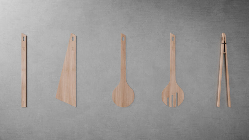 Five wooden kitchen utensils, including a spatula, knife, spoon, slotted spoon, and tongs, are arranged in a row against a gray textured background