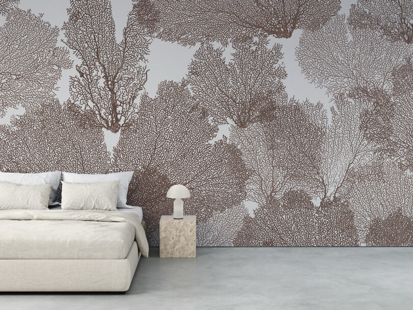 A minimalist bedroom with a beige bed, a small stone side table with a lamp, and a large wall mural featuring intricate brown coral patterns
