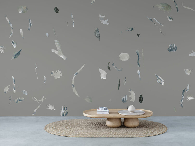 A minimalist room with a round woven rug, a low wooden coffee table, and a gray wall decorated with scattered abstract shapes