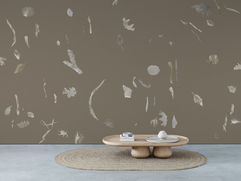 A minimalist room with a round woven rug, low wooden coffee table, and abstract-patterned wallpaper on a taupe wall.