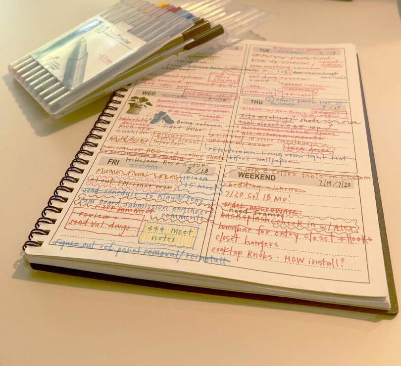 Open planner notebook with handwritten tasks in various colored pens, many crossed out, next to a set of colored fineliners on a beige table—styled in the creative spirit of Nicki Gitlin.