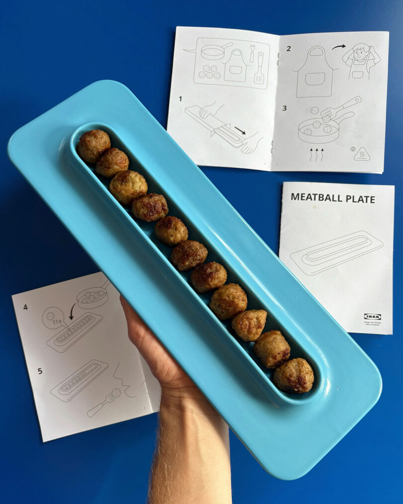 A hand holds a blue plate with a row of meatballs; IKEA-style instructions are displayed on the blue table in the background.