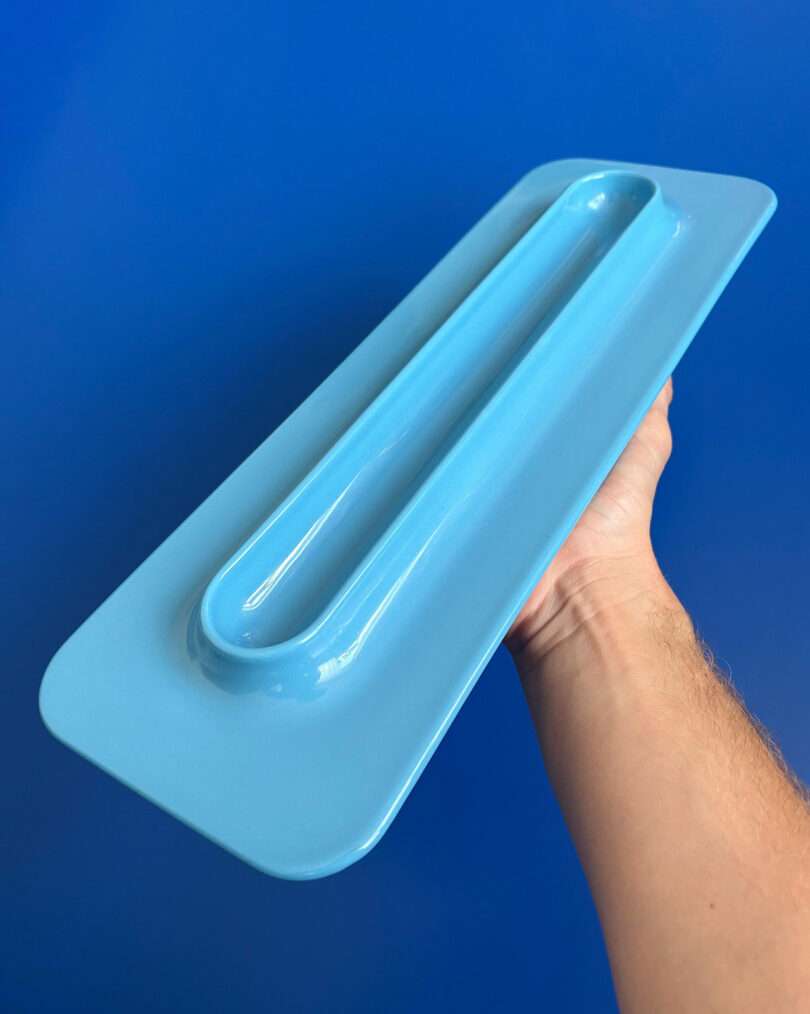 A person holds a blue rectangular plastic object with a raised handle against a solid blue background.