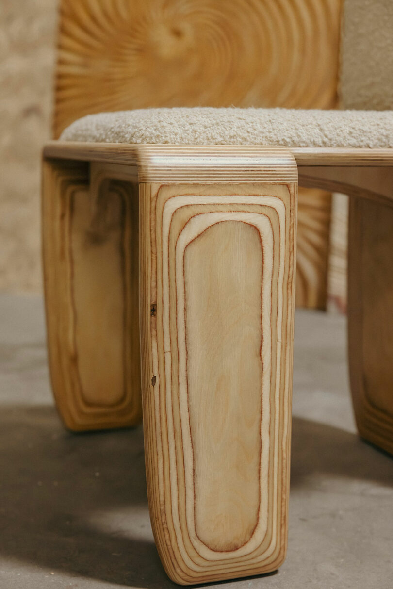 Close-up of a wooden chair leg with visible wood grain patterns and a cushioned seat, inspired by Kelly Wearstler's signature style, set against a background featuring similar wood textures.