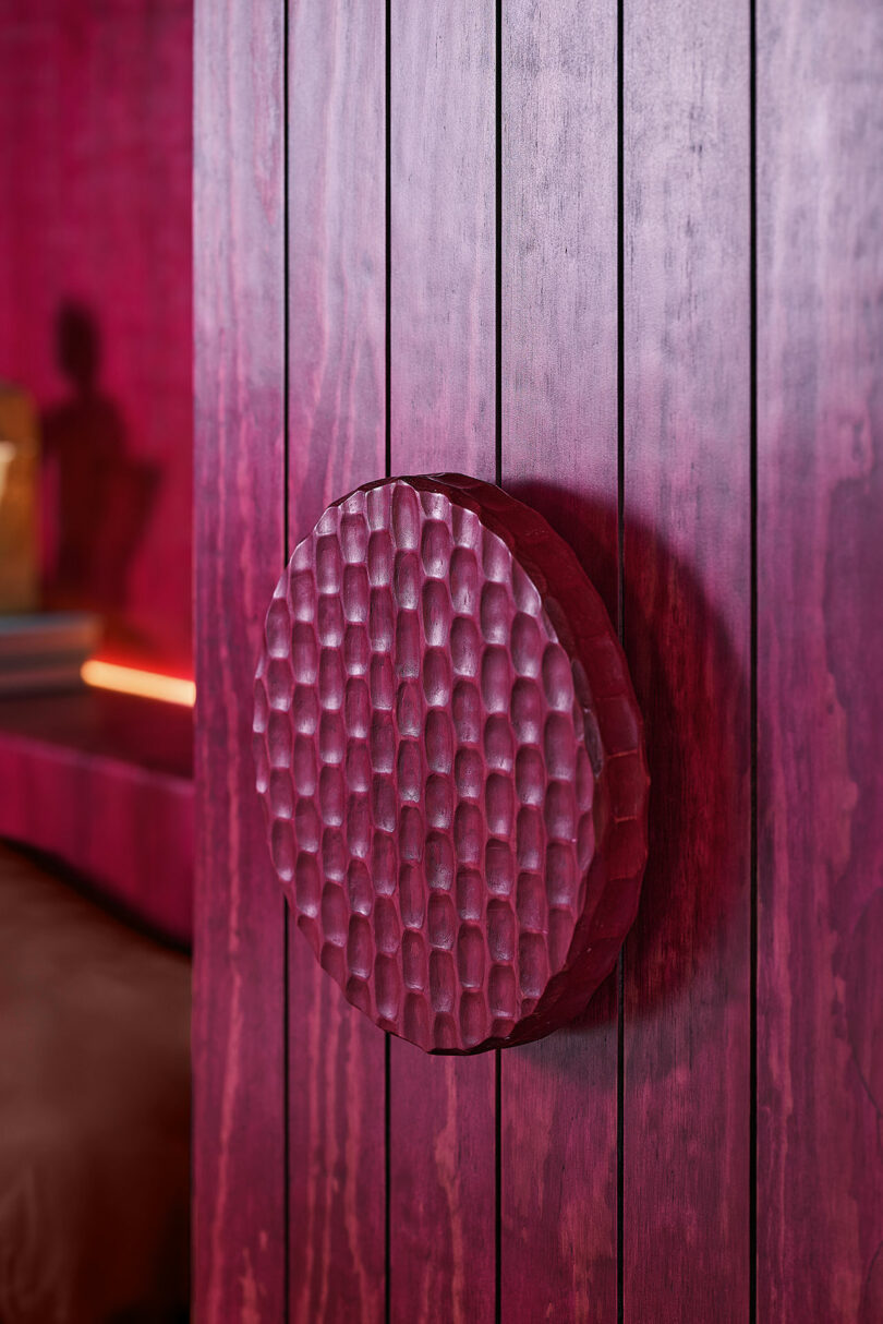 A textured, circular maroon handle is mounted on a vertical panel of matching maroon wood.