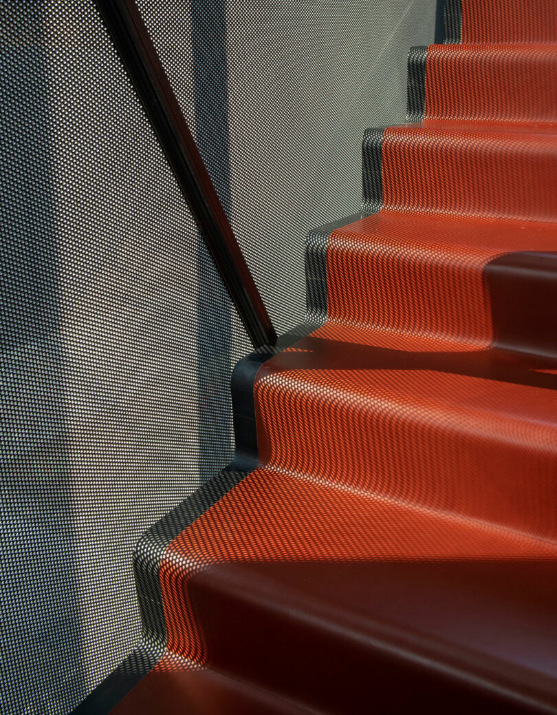 Red steps beside a perforated metal railing create a pattern of light and shadow on the stairway.