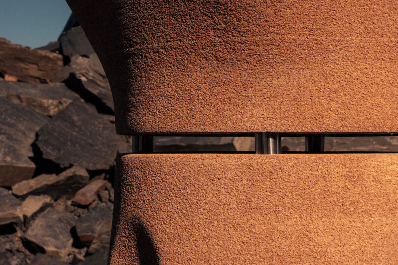 Close-up of a textured, terracotta-colored structure with a metal rod in the center, set against a background of dark, jagged rocks