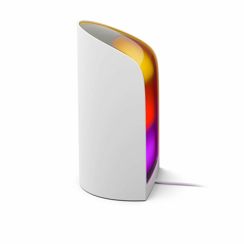 A white, curved, vertical Hue device with a translucent front displaying orange, yellow, and purple lights, connected by a power cord.
