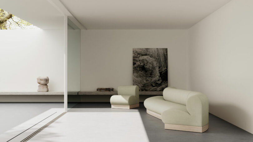 Minimalist living room with light beige curved sofa and chair, a low concrete bench, abstract artwork, and a small sculpture on display. The neutral color palette feels as soft as candy floss beside the spacious large window.