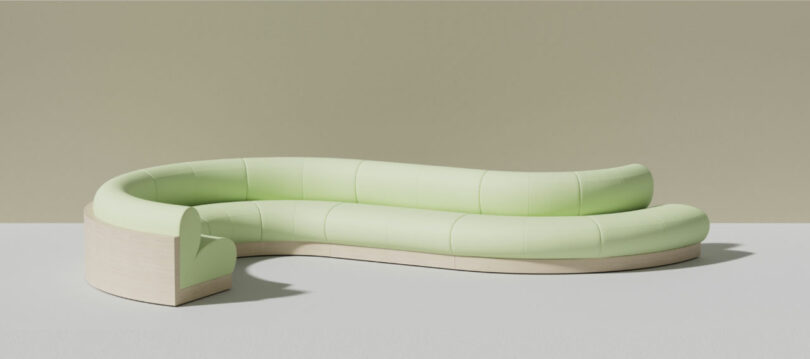 Curved, light green upholstered sofa with a candy-inspired hue and light wood base set against a plain beige background.