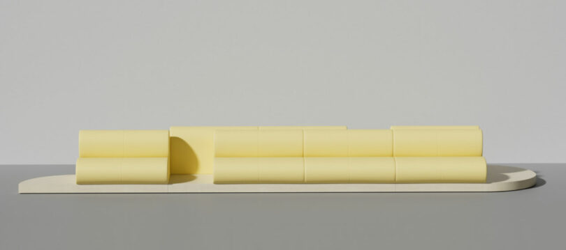 A minimalist arrangement of pastel yellow, candy-like rounded rectangular blocks placed on a light, flat base against a plain gray background.