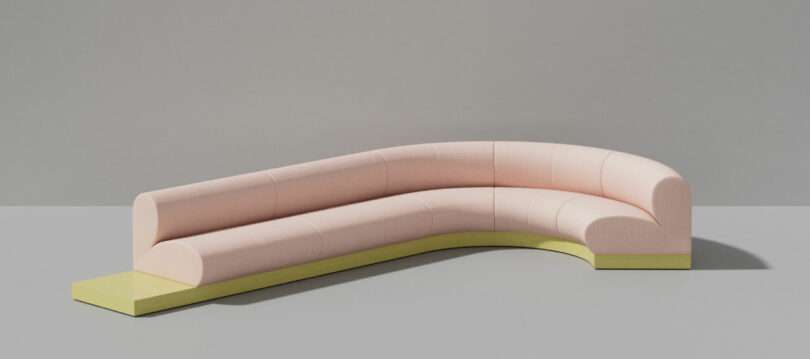 Curved, candy-pink upholstered sectional sofa with a low yellow base, set against a plain grey background.