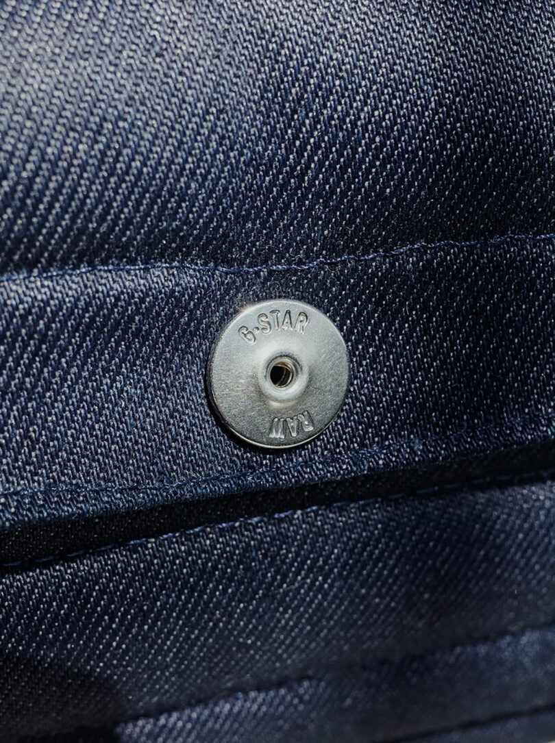 Close-up of a metal snap button on dark blue fabric, with 