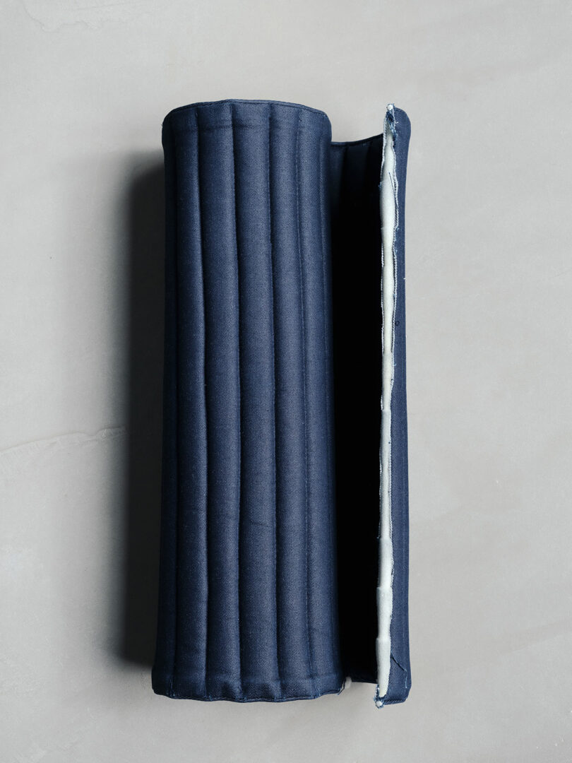 A dark blue, ribbed, rectangular object with a vertical opening on one side, revealing a white interior, placed on a light surface.