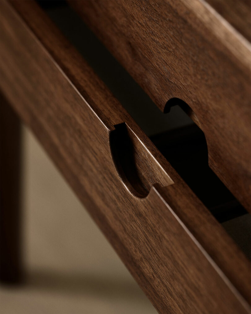 Close-up of a wooden drawer designed by Kai Kristiansen, with a curved cutout handle, partially open to reveal the rich texture and grain of the wood.