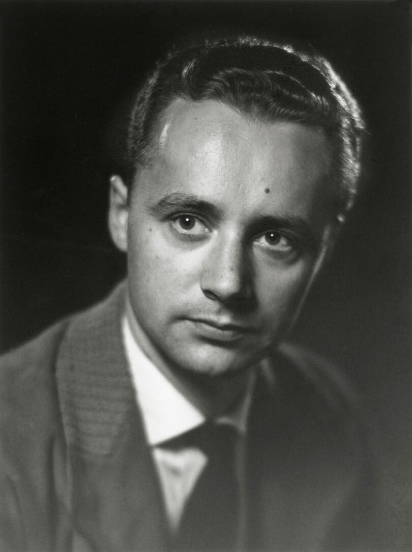 Black and white portrait of a young man in a suit and tie, looking slightly to the side with a neutral expression against a dark background, evoking the timeless style of Kai Kristiansen.