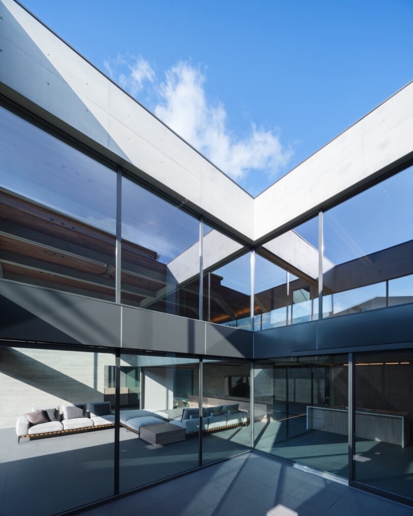 Modern building with large glass windows, exposed concrete, and minimalistic outdoor seating, featuring open courtyard under a clear blue sky.
