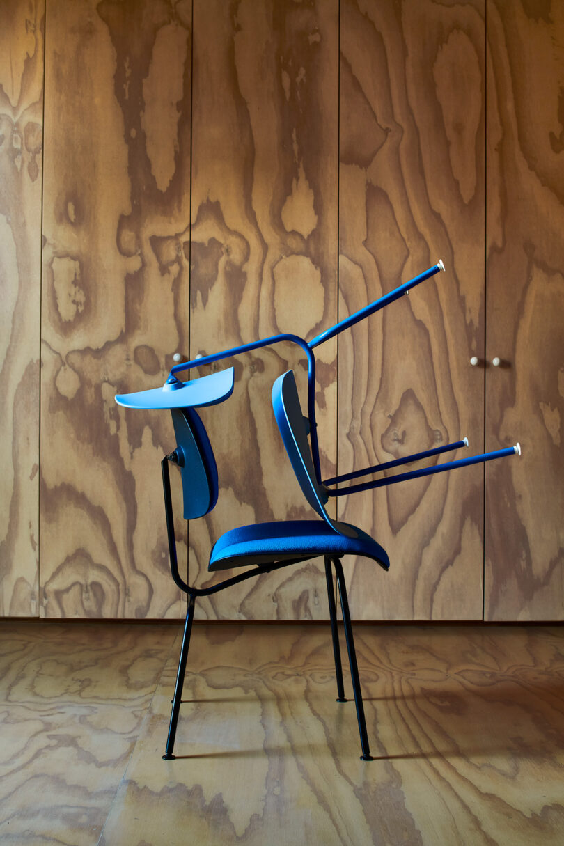 A modern chair with blue upholstery and two crutches balanced across its backrest, set against a wooden paneled wall.