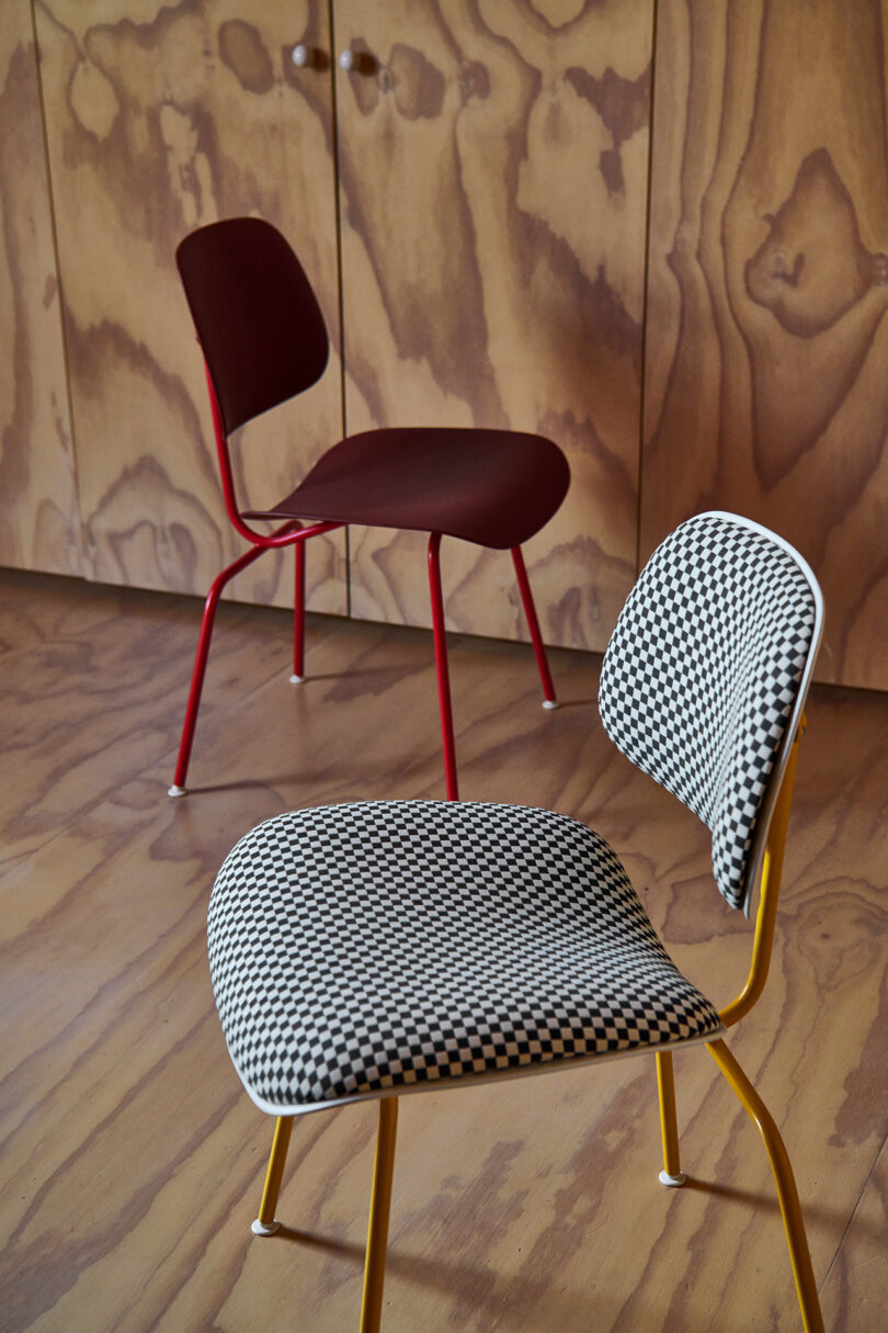 Two modern chairs are placed on a wooden floor; one has a red frame and seat, while the other has a yellow frame with a black-and-white checkered seat and backrest.