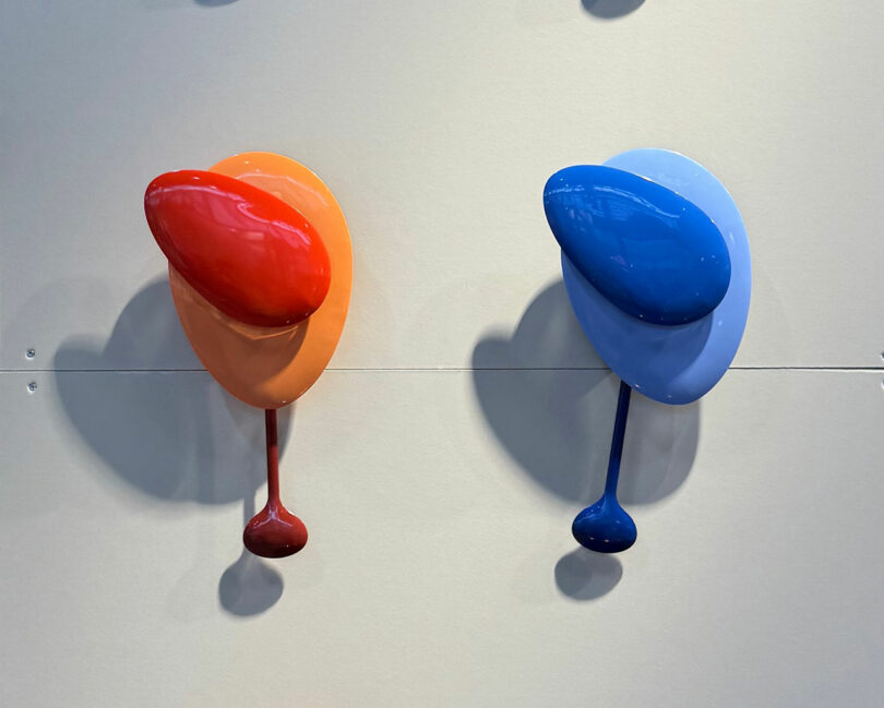 Two glossy, abstract wall sculptures showcased at Maison & Objet feature rounded shapes—one in red and orange, the other in blue and light blue—both strikingly mounted on a plain wall.