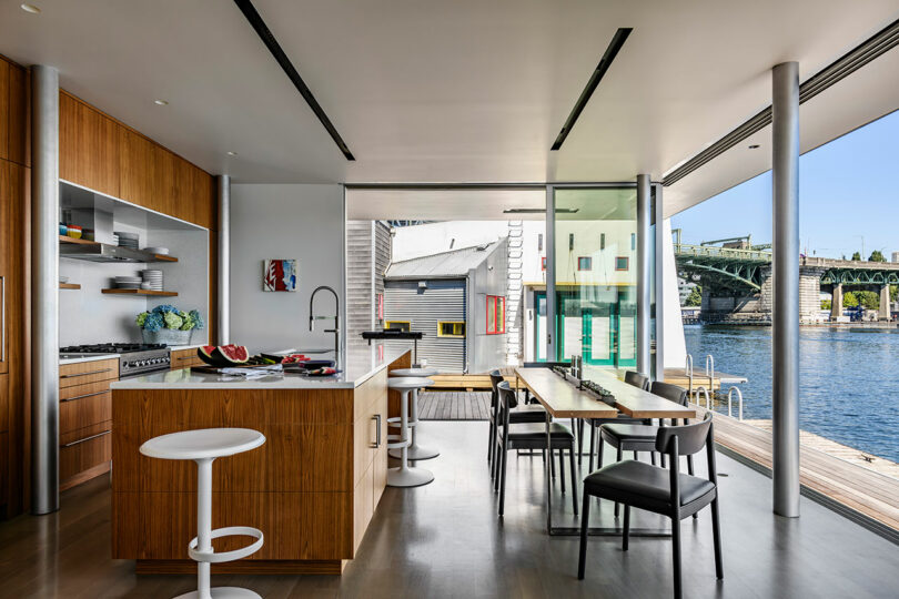 Modern kitchen and dining area with wood finishes, large windows, and a view of a river and bridge outside.