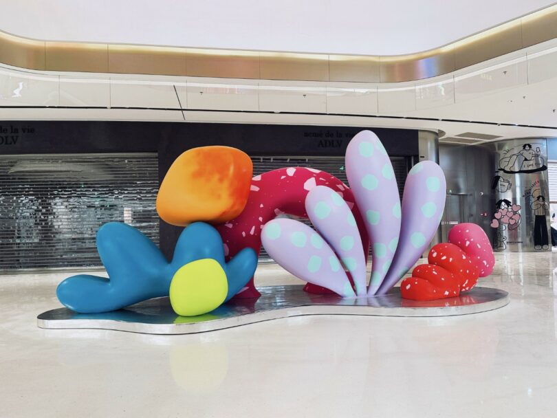 Colorful abstract sculpture by Studio Proba features large rounded shapes in blue, green, orange, red, pink, and purple, displayed on a shiny floor in a modern indoor space