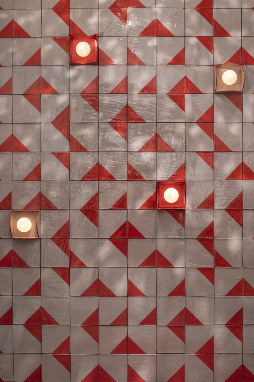 Red and gray patterned tiles with geometric triangles on a wall, featuring four round lights spaced across the surface