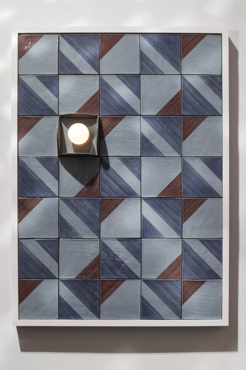 Rectangular arrangement of blue and maroon geometric tiles with a wall-mounted light fixture positioned over two tiles near the upper left corner