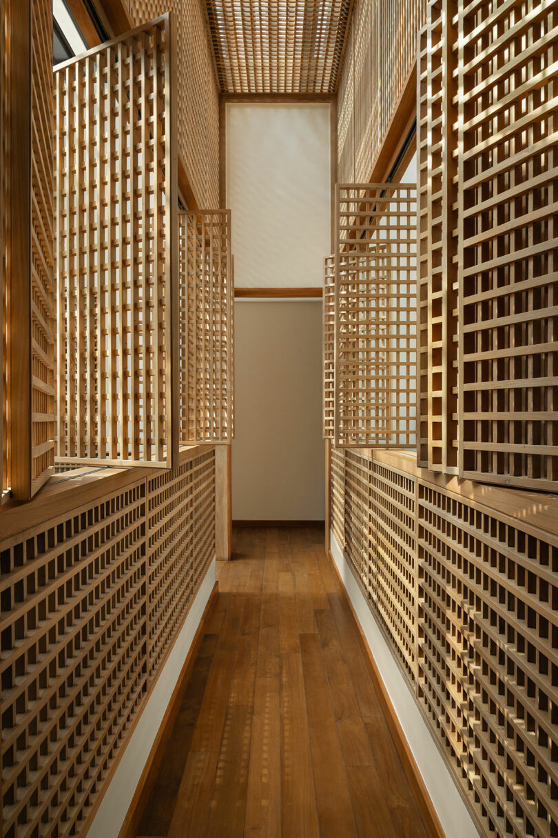 A hallway with wooden lattice walls and windows, wooden floors, and natural light streaming in from above.