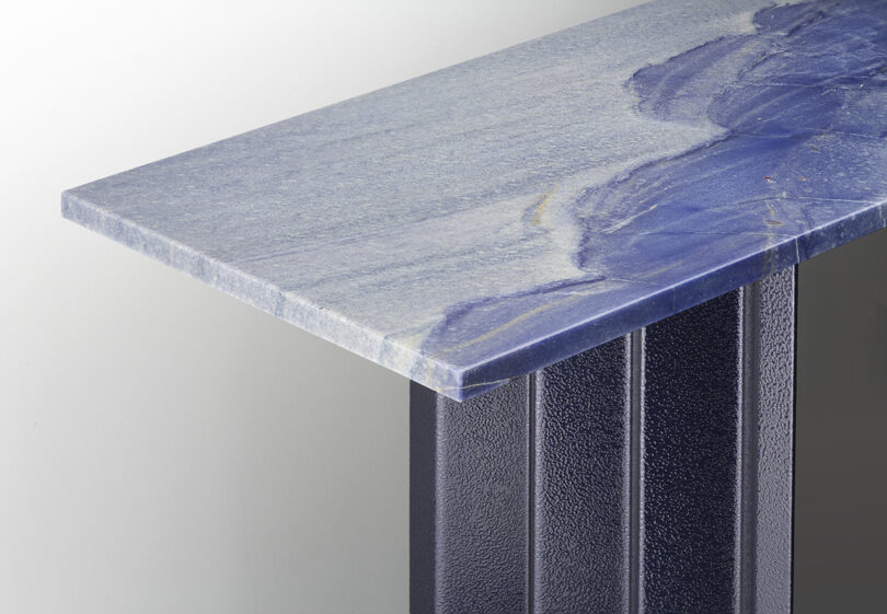 A close-up view of a table with a polished blue stone top and a textured, dark vertical support beneath.