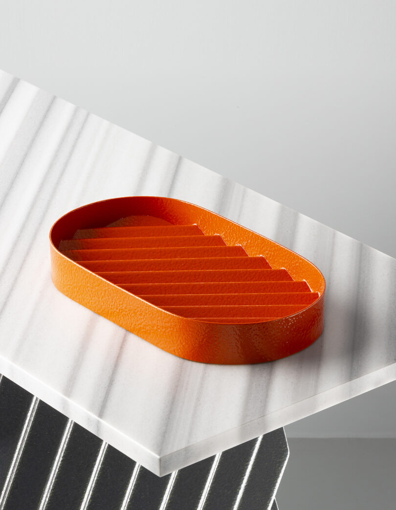 An orange textured oval tray with ridged interior rests on a white marble surface with gray veins.