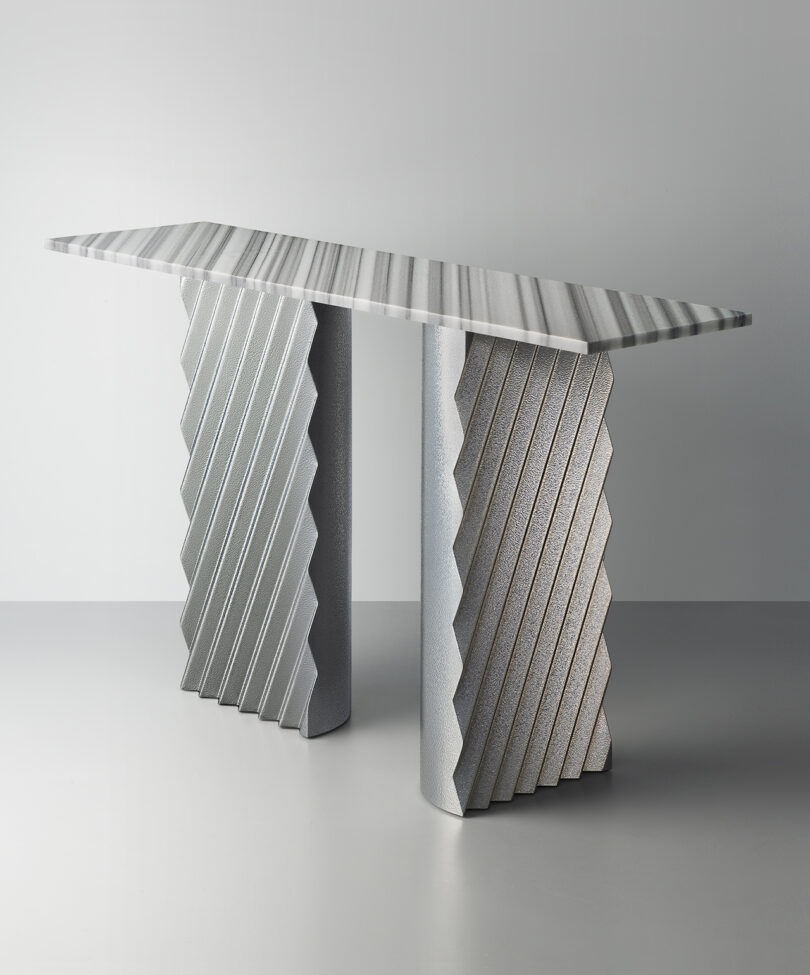 A modern console table with a striped rectangular top and two textured, zigzag-patterned legs, set against a plain grey background.