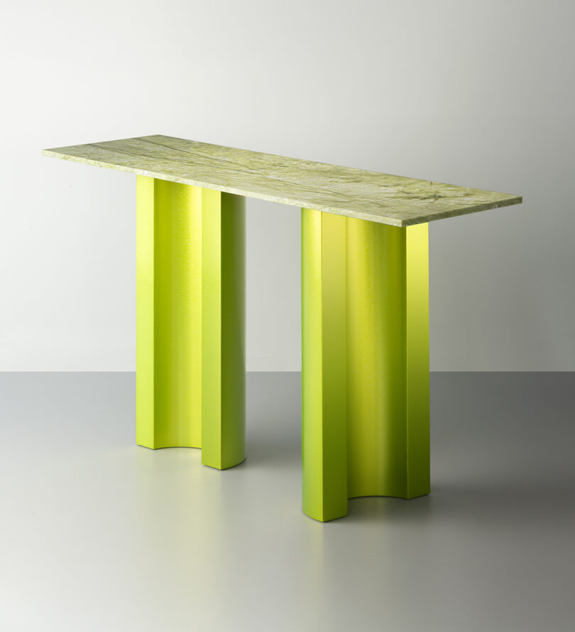 A modern console table with a light green textured top and three bold, curved, bright green legs, set against a plain background.