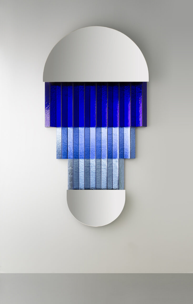 Wall-mounted abstract artwork featuring two semicircular mirrors and rows of blue gradient glass panels arranged vertically in the center.