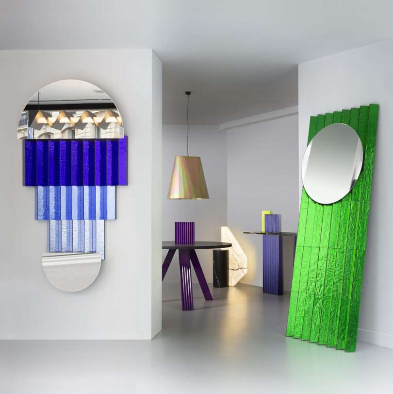 Modern interior with geometric furniture, colorful textured panels, round mirrors, and a hanging iridescent pendant light in a minimal white room.