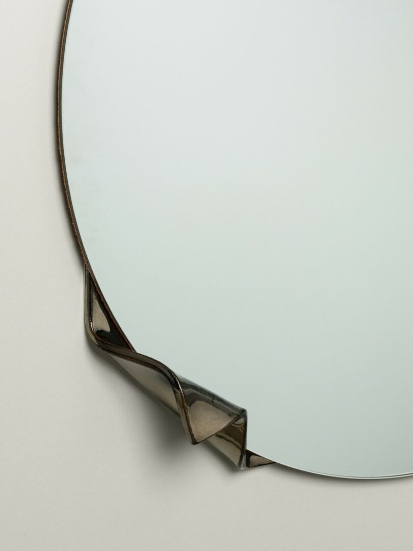 A round mirror with a small section of its metal frame bent outward at the lower left edge, set against a plain background