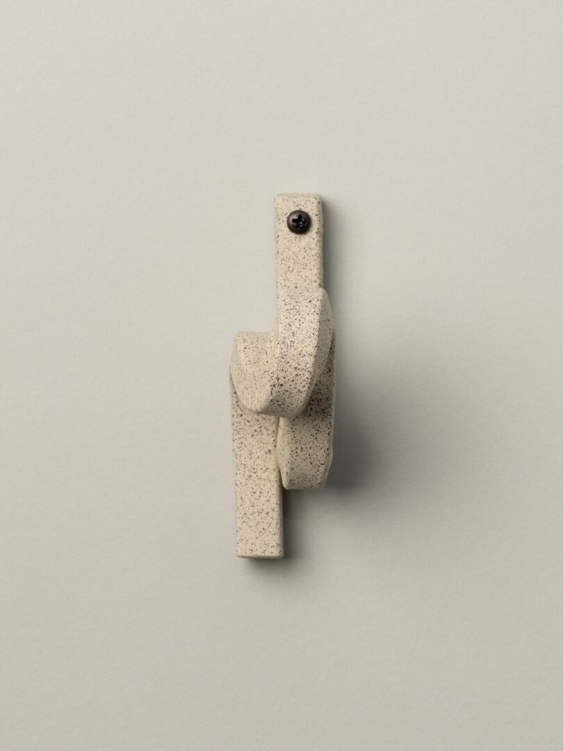 A textured, beige ceramic sculpture with a single black screw mounted on a plain light gray background