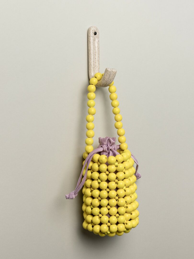 A small yellow beaded bag with a purple drawstring pouch inside, hanging from a wall hook against a neutral background