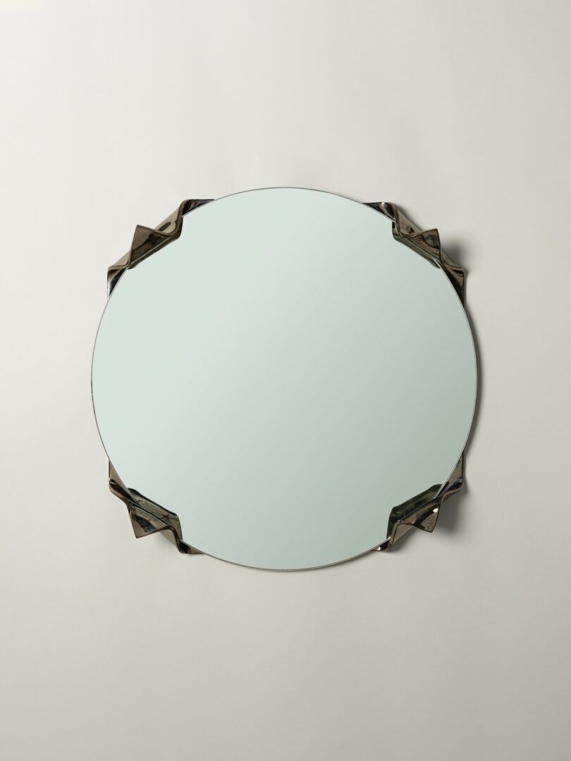 Oval mirror with beveled glass edges and four metallic decorative brackets, mounted on a plain light-colored wall