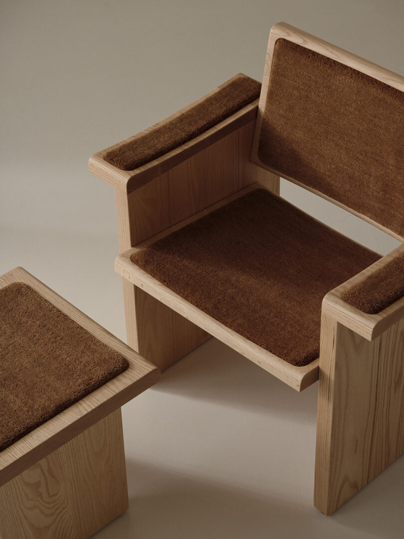A wooden chair and side table with brown textured cushions on the seat, backrest, armrests, and tabletop, set against a neutral background.