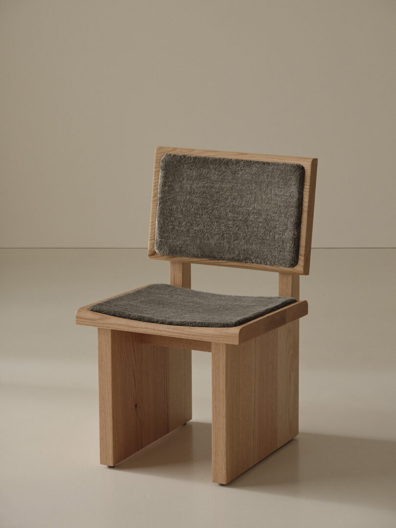 A wooden chair with a minimalist design, featuring a rectangular backrest and seat, both cushioned with gray fabric upholstery.