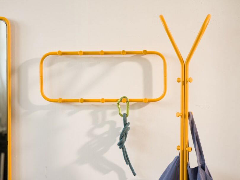 A yellow wall-mounted rack with a blue rope tied to a green carabiner and a yellow coat stand holding a blue bag.