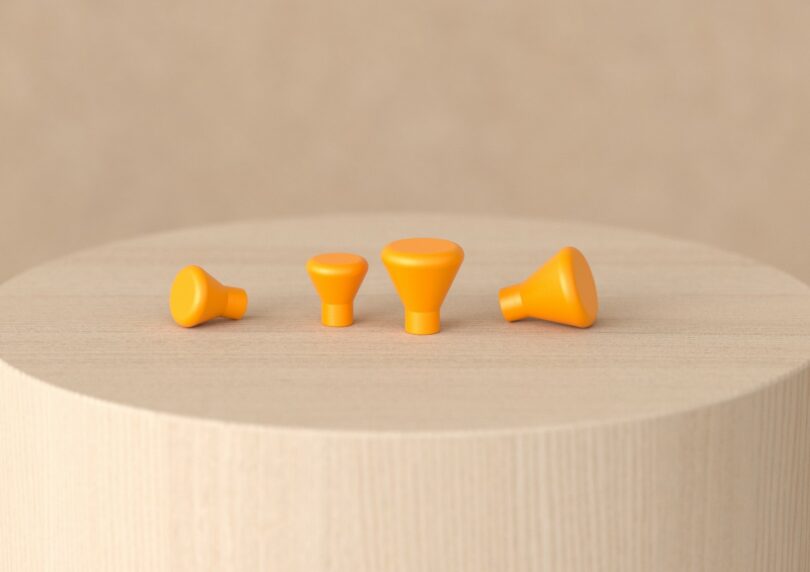 Four orange, cone-shaped knobs of varying sizes are arranged in a row on a light wooden circular surface with a neutral background