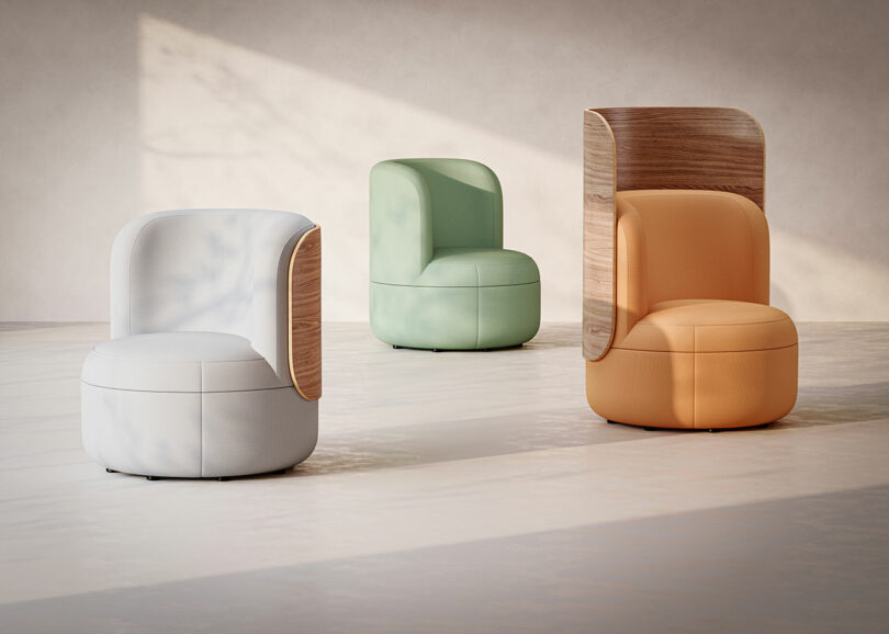 Three modern armchairs, each in white, mint green, and orange, with smooth upholstery and wooden accents, are arranged in a minimalist room with soft natural light.
