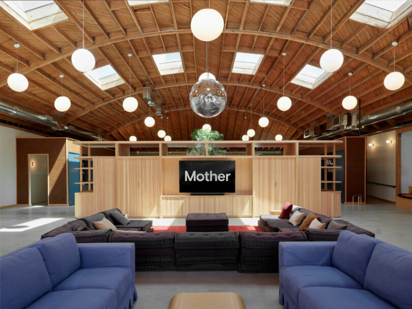 Spacious lounge with blue and black sofas, wooden ceiling, globe lights, a disco ball, and a large screen displaying 