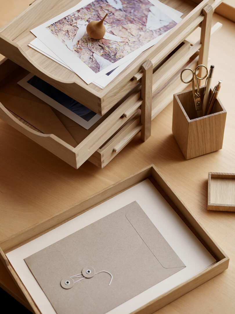 A wooden desk organizer holds papers, envelopes, and a pencil holder with scissors and pens on a light wood desk.