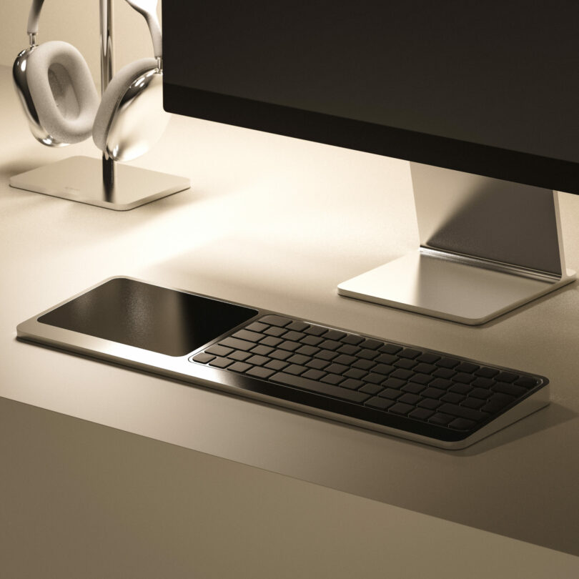 A modern computer workstation featuring a monitor, wireless keyboard with an integrated touchpad, and a pair of headphones on a stand.