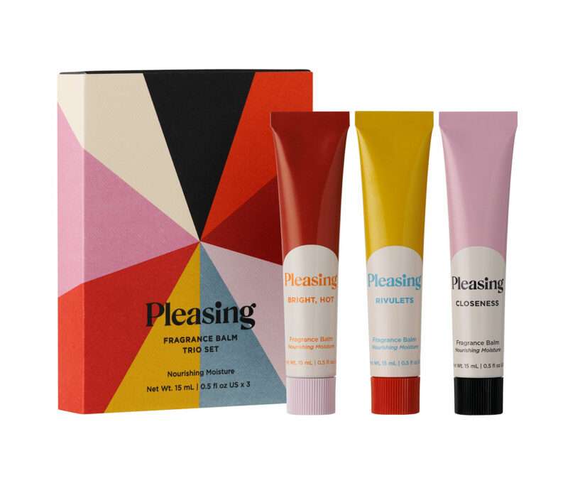 Three tubes of Pleasing fragrance balm (red, yellow, pink) stand beside a colorful geometric box labeled 